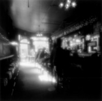 This is an misty old fashioned shot of a bar. It has ghostly looking people sitting on stools. they are ethereal transparent images. The light is filtering in through a window and falling on the bar. It looks like it could be anytime between 1930's to the present. The little lights are twinkling around the bar. While the people look like ghosts the overall feeling is warm and pleasant.