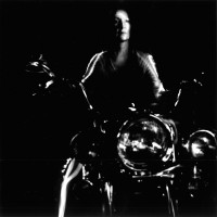 Stephanie belongs to the same motorcycle club I do. The image looks as if she is about to take off from a stop light on a big Harley. perhaps she is pensively trying to paddle the bike around a parking lot. She has a determined look on her face. The light unifies her figure with parts of the bike, but it is unclear exactly where she is.